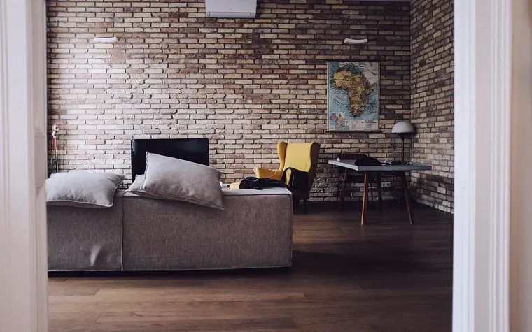 Salon avec un canapé, un fauteuil jaune et un mur de briques